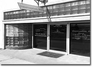 Black-and-white photo of a storefront with an Intervention, Inc. sign and the office hours on the window