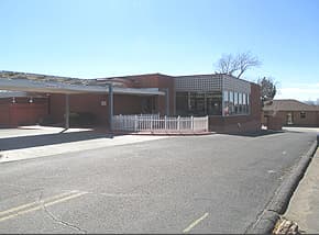The single-story brick ICCS Pueblo building with a white fence and parking lot