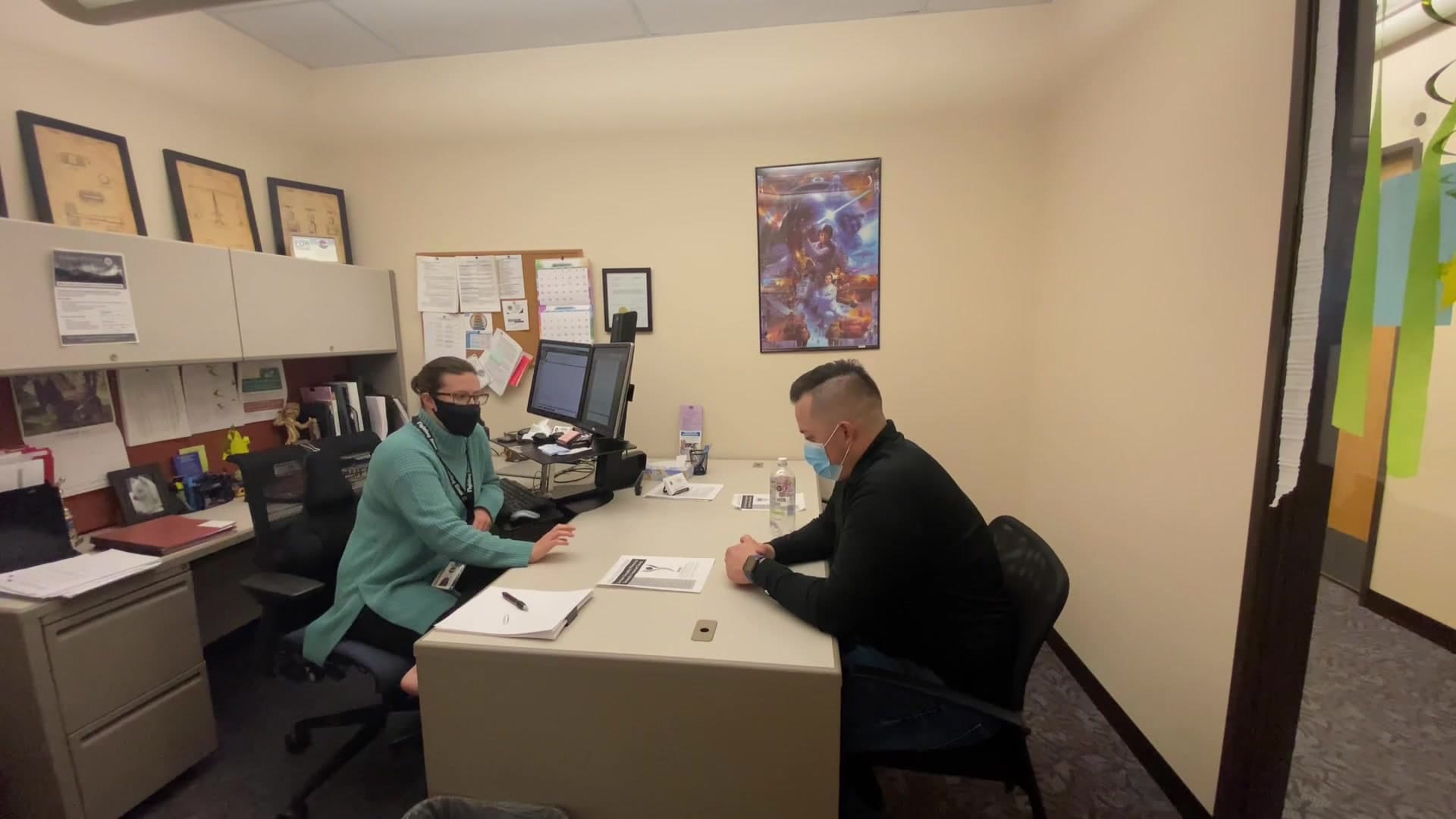 Still from the SAVE Panel Referral video: two people in face masks talk across an office desk