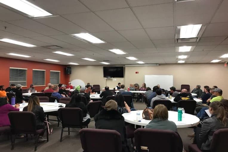 A Survivor Empathy Panel audience seated at round tables in a meeting room, facing the panel at the front