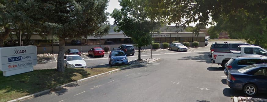 Low office building with an Intervention, Inc. sign, seen across a tree-lined parking lot